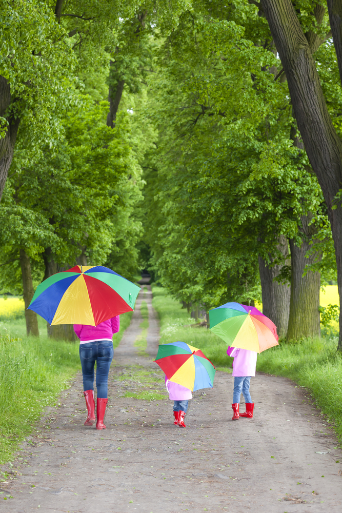 mother and her daughters with umbrellas in spring alley